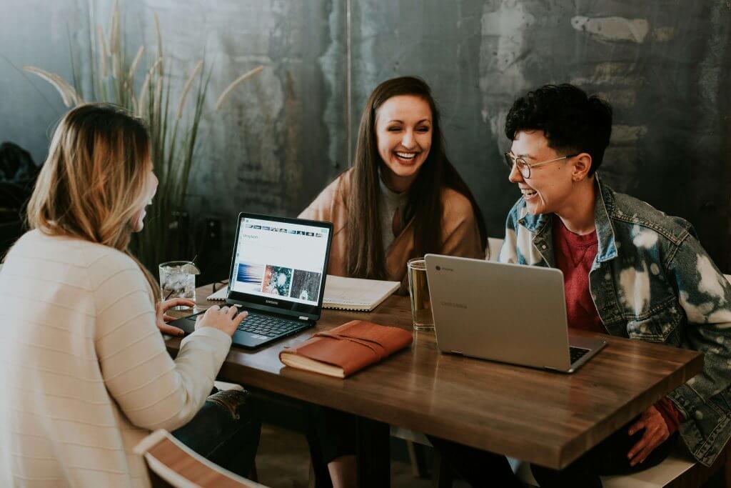 Three colleagues chatting at a table with laptops